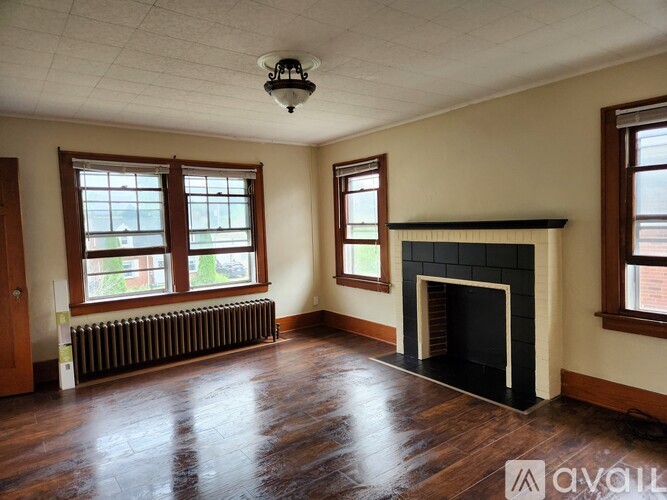 A large empty room with a fireplace and two windows.