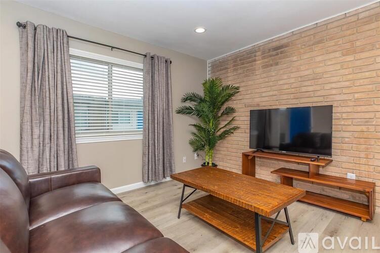 A living room with a brown leather couch, a wooden coffee table, and a flat-screen TV mounted on a brick wall.