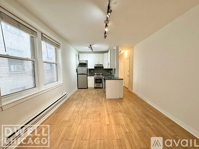 A well-lit, empty apartment with wood flooring and a kitchenette.