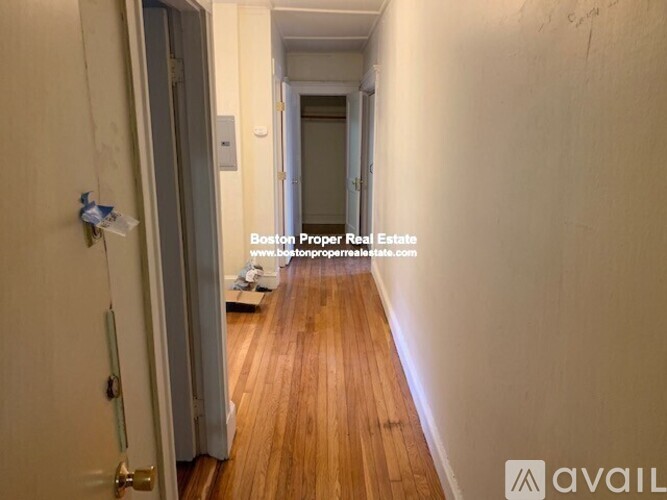 A hallway with wooden floors and white walls, leading to a door at the end.
