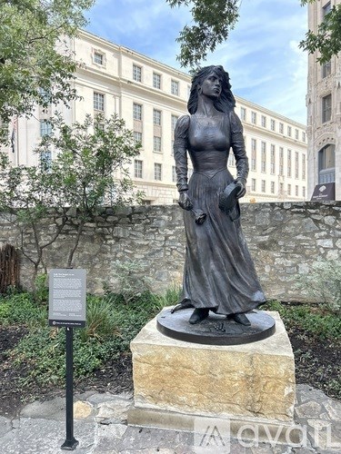 A statue of a woman stands on a stone pedestal in front of a building.