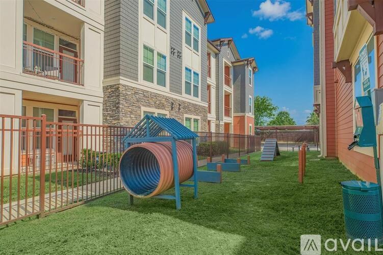 A playground area with a slide and a tunnel in the foreground in front of apartment buildings.