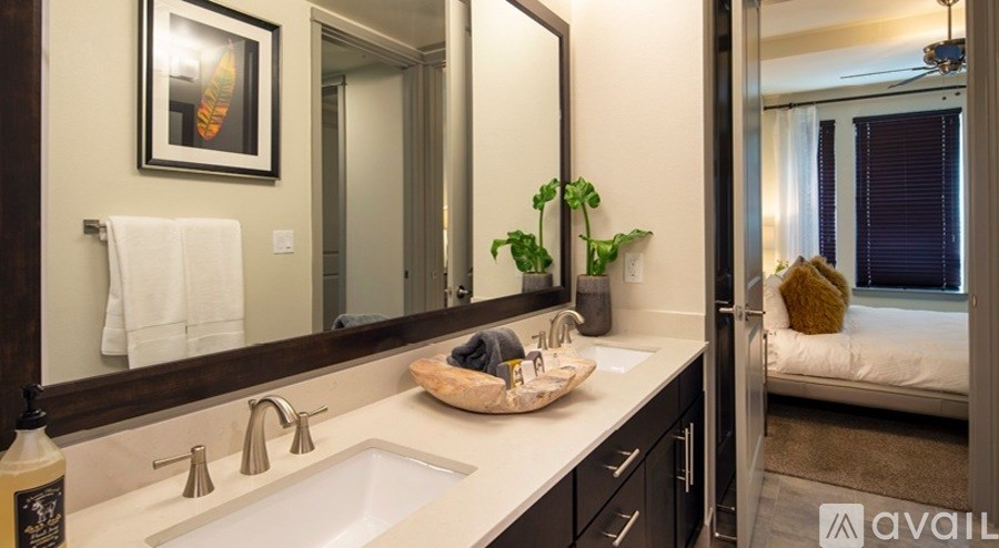 A bathroom with a sink, mirror, and a bed in the background.