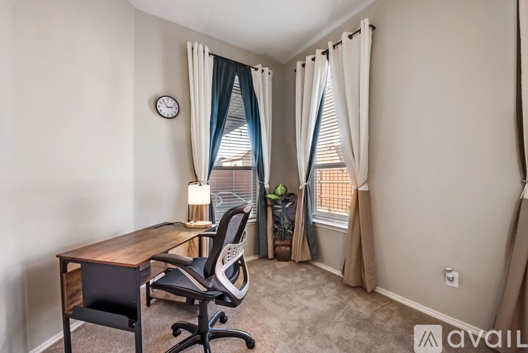 A room with a desk and chair in front of a window with curtains.
