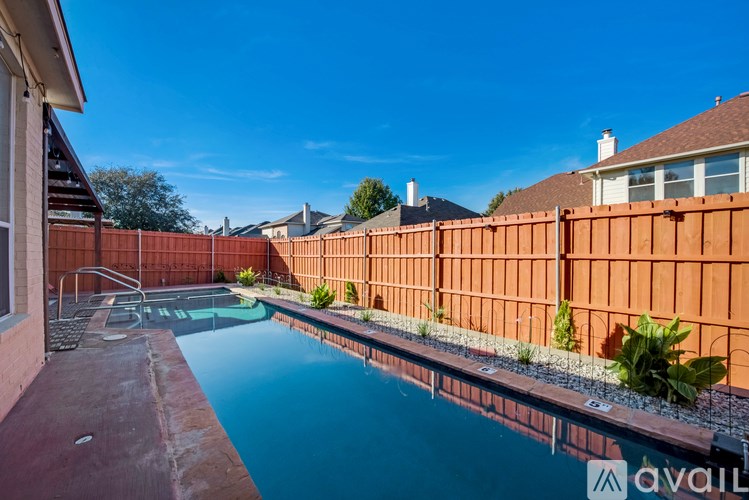 A pool surrounded by a red fence with a house in the background.