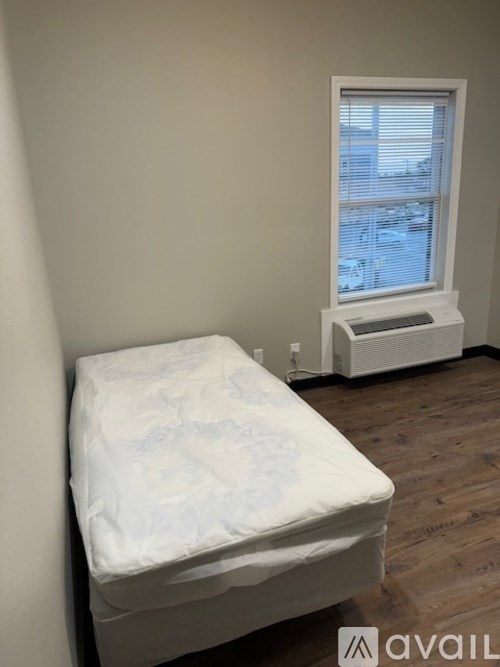 A white mattress is on a wooden floor in a room with a window.
