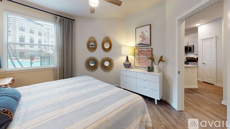 A bedroom with a large bed, a window with a view of a building, and a white dresser with a mirror above it.