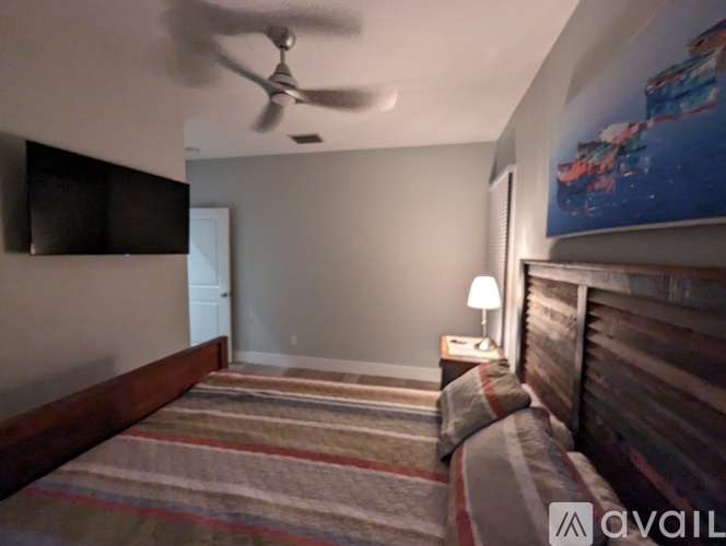 A bedroom with a bed, a ceiling fan, and a painting on the wall.