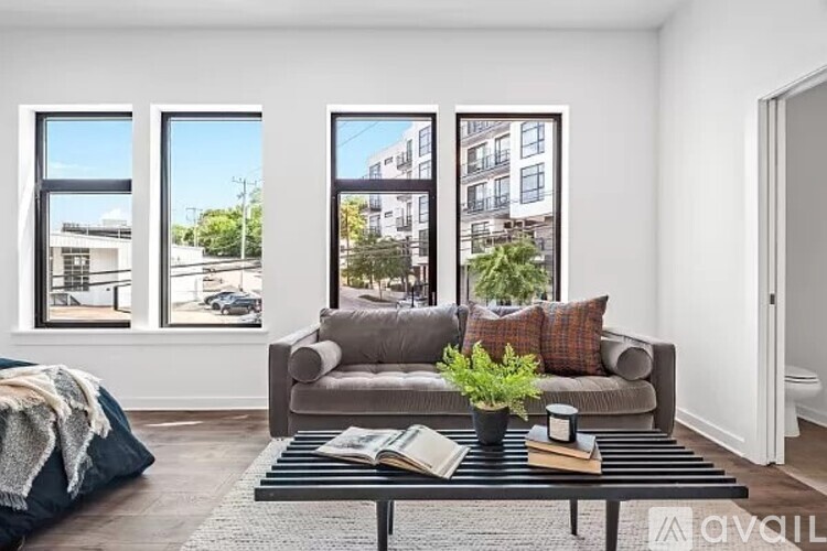 A living room with a grey couch, a black coffee table, and a large window with a view of the street.