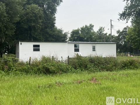 A white building with a black window is surrounded by greenery.