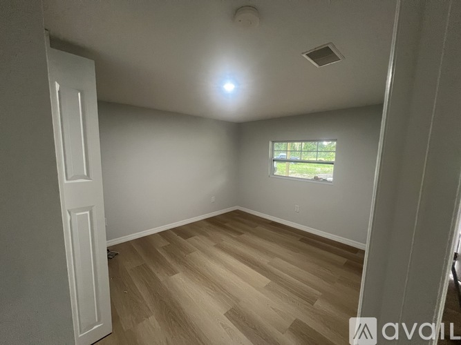 A room with wooden flooring and a window showing greenery outside.