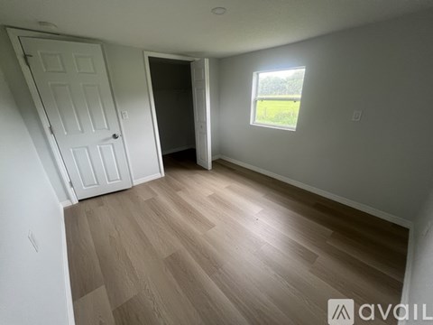 A room with wooden flooring and a window showing a green field outside.