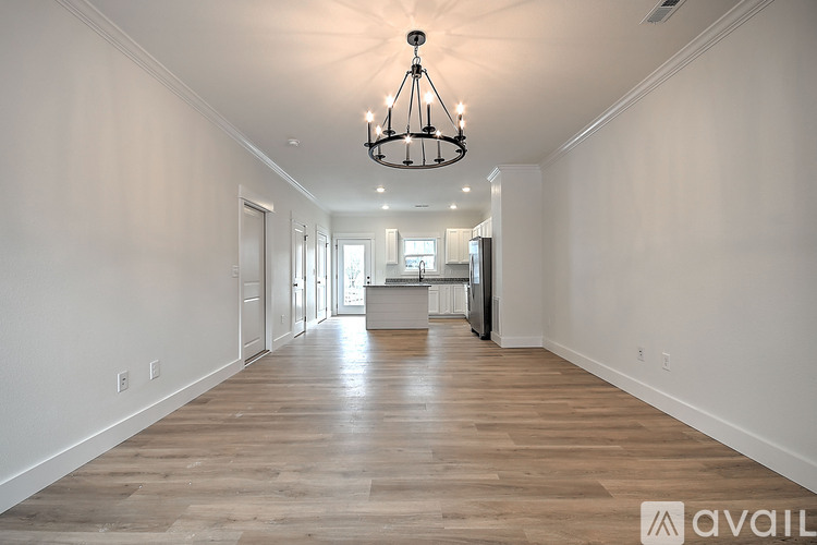 A long hallway with a chandelier and wooden floors.