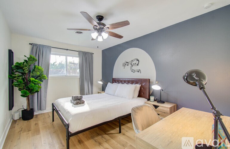 A bedroom with a bed, a chair, a ceiling fan, and a window with curtains.