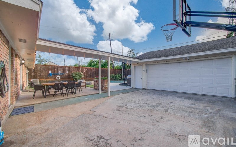 A basketball hoop is installed in a backyard with a patio and a dining table.