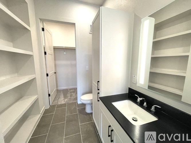 A bathroom with a toilet, sink, and shelves.