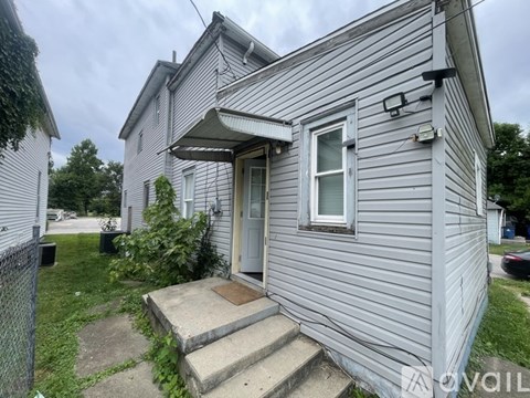 A house with a grey siding and a white door is for sale.