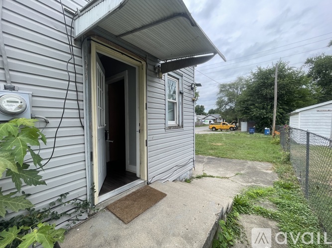 A grey house with a door open and a mat on the concrete.