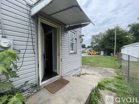 A grey house with a door open and a mat on the concrete.