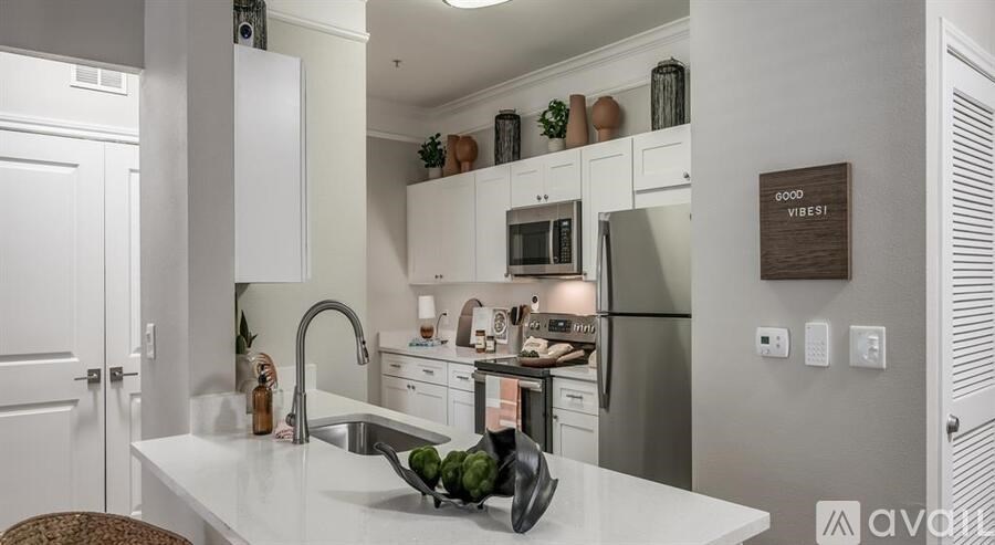 A kitchen with white cabinets and a white countertop with a sink and a bowl of fruit on it.