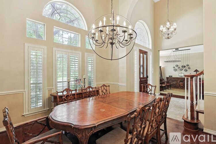 A large wooden dining table with chairs and a chandelier hangs in a spacious dining room.