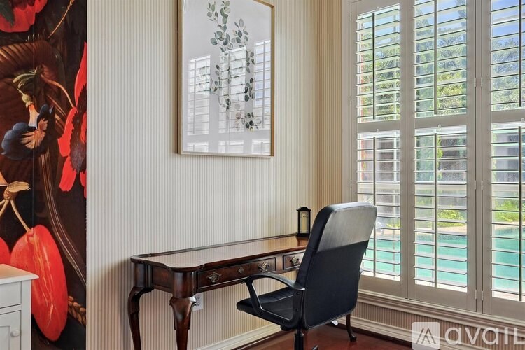 A desk with a chair in front of a window with blinds.
