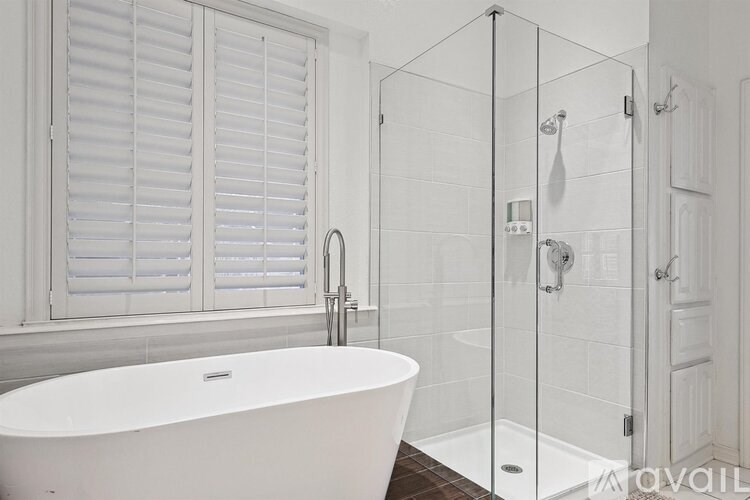A white bathroom with a tub, shower, and closed white shutters.