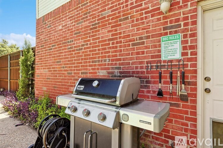A BBQ grill is on a stand outside a brick building with BBQ rules posted on a sign.