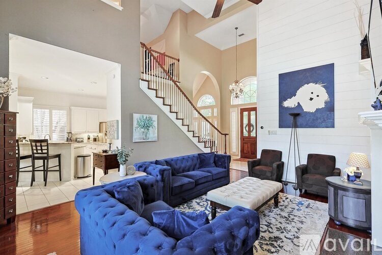 A living room with a blue couch and a painting of a white ghost on the wall.