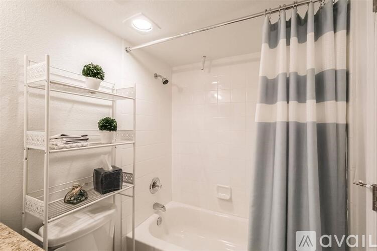 A bathroom with a white tub, grey shower curtain, and a shelf with plants and toiletries.