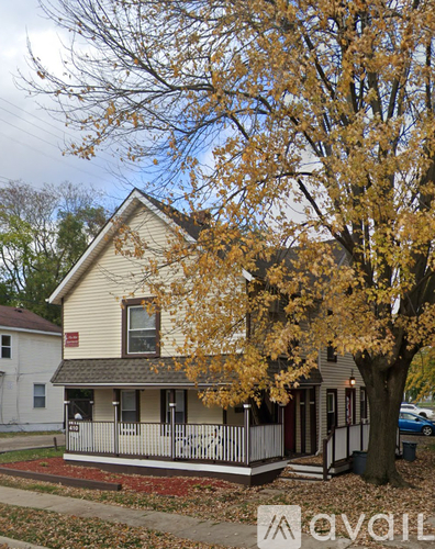 A house with a porch and a tree with yellow leaves.