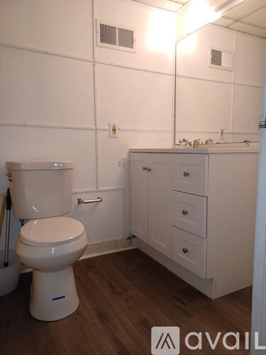 A white toilet in a small bathroom with wooden floors and white walls.