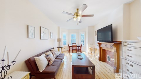 A living room with a brown couch and a television on top of a wooden cabinet.