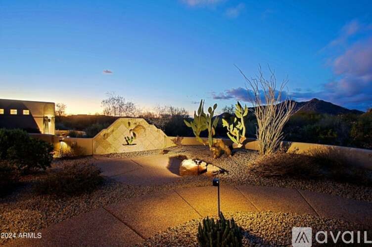 A garden with a pathway and a building in the background is illuminated by lights.
