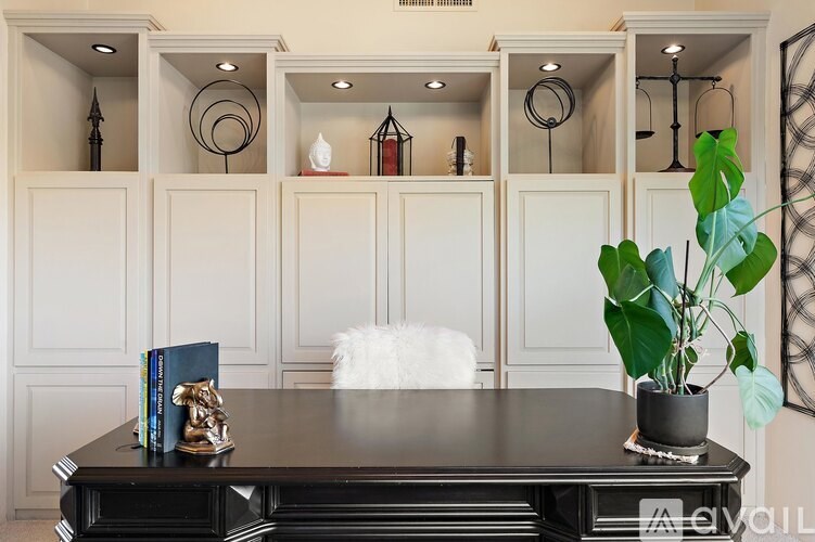 A black piano with a plant on top and a white chair in front of a wall with shelves.