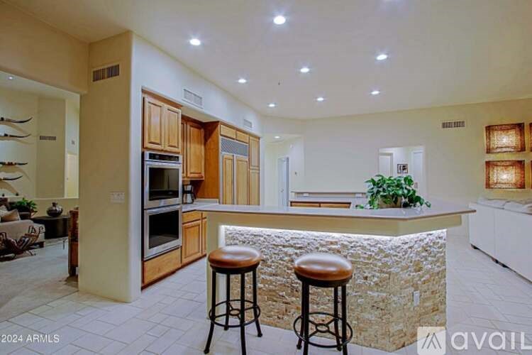 A kitchen with a bar stool in front of a stone backsplash.