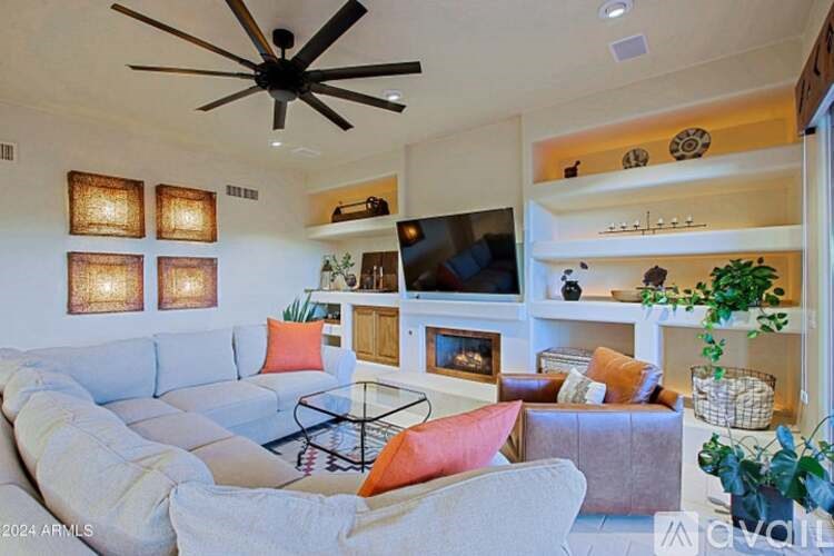 A living room with a white couch, a glass coffee table, and a ceiling fan.