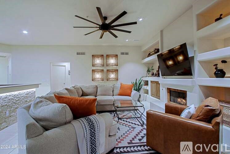 A living room with a grey couch, a brown armchair, a coffee table, a fireplace, and a ceiling fan.