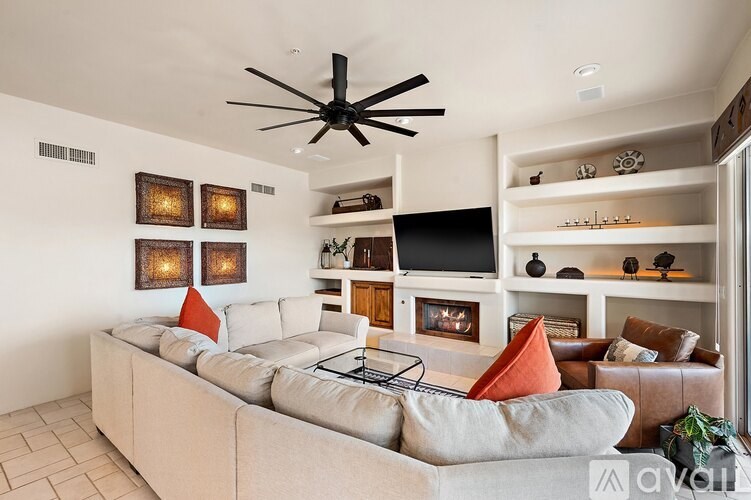 A living room with a beige couch and a black ceiling fan.