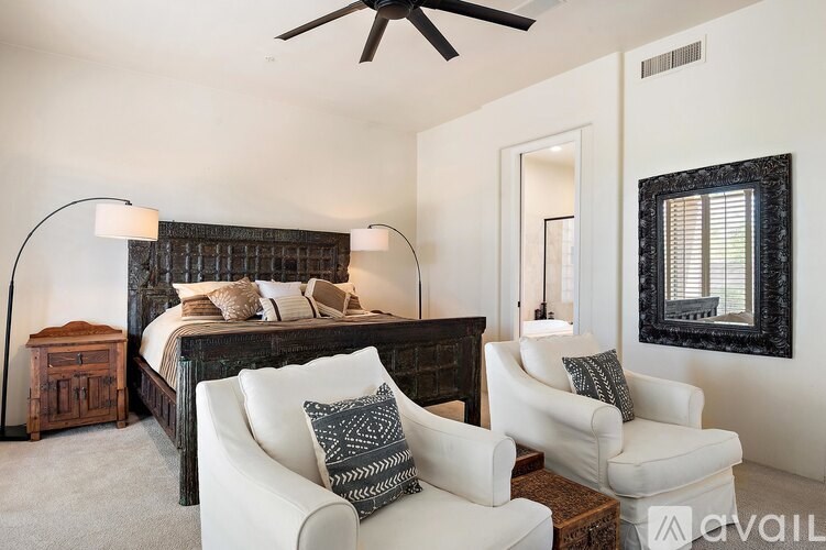 A bedroom with a large bed and a white chair.