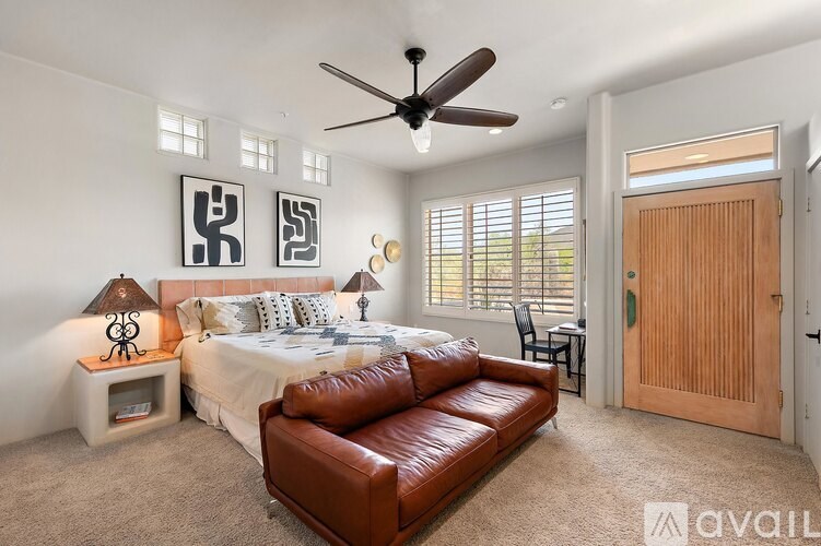 A bedroom with a bed, a brown leather couch, and a ceiling fan.