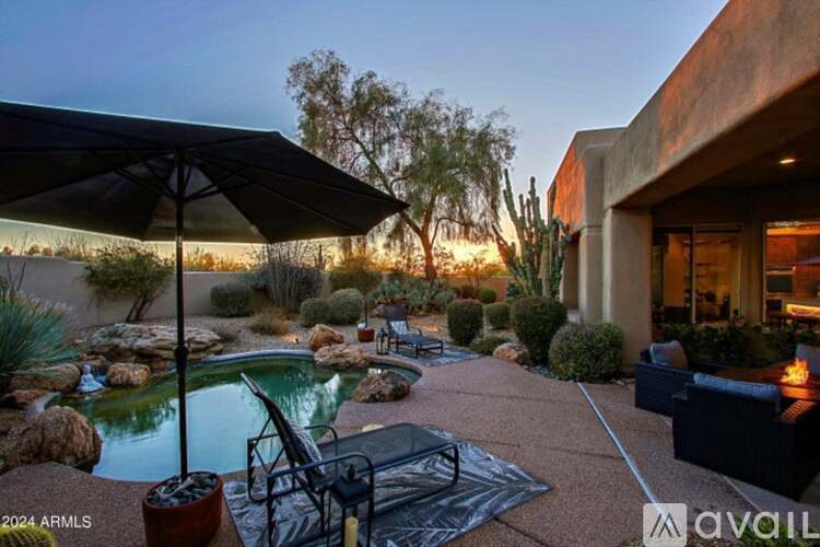 A pool surrounded by rocks and plants with a patio and umbrella.