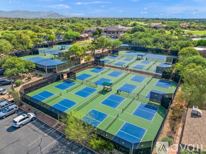 A tennis court complex with multiple courts surrounded by trees and buildings.