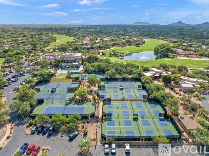 A large outdoor tennis court surrounded by a parking lot.