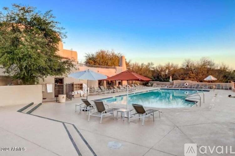 A pool area with chairs and a tree in the foreground.