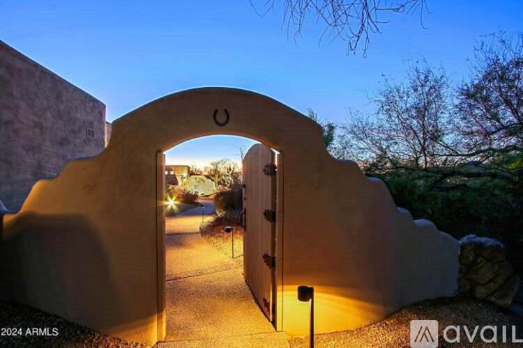 A stone archway entrance to a home with a lit pathway leading to it.