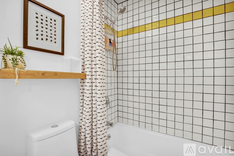 A bathroom with a white toilet and a shower with a yellow stripe.