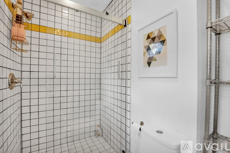 A bathroom with a white tiled shower and a picture on the wall.