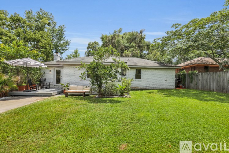 A house with a white exterior and a brown roof is surrounded by a green lawn and trees.