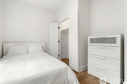 A white bedroom with a bed, dresser and wardrobe.